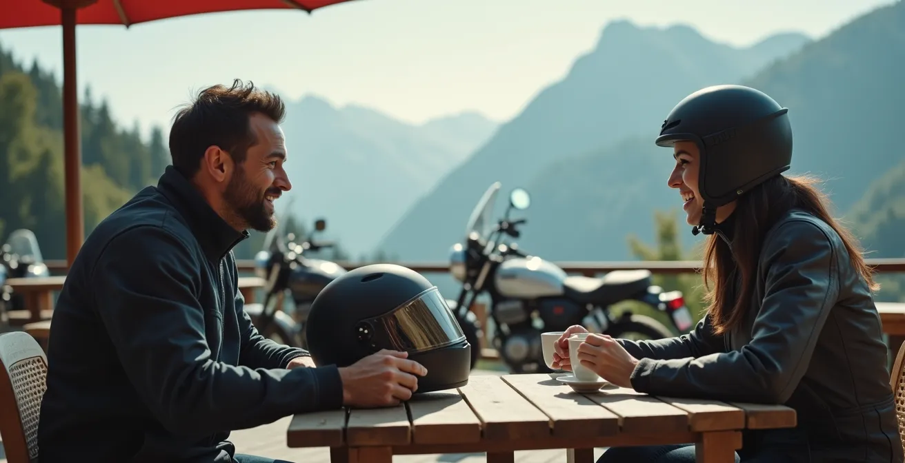 Couple de motards en pause café, casques posés sur la table, sourires complices après une conversation en route